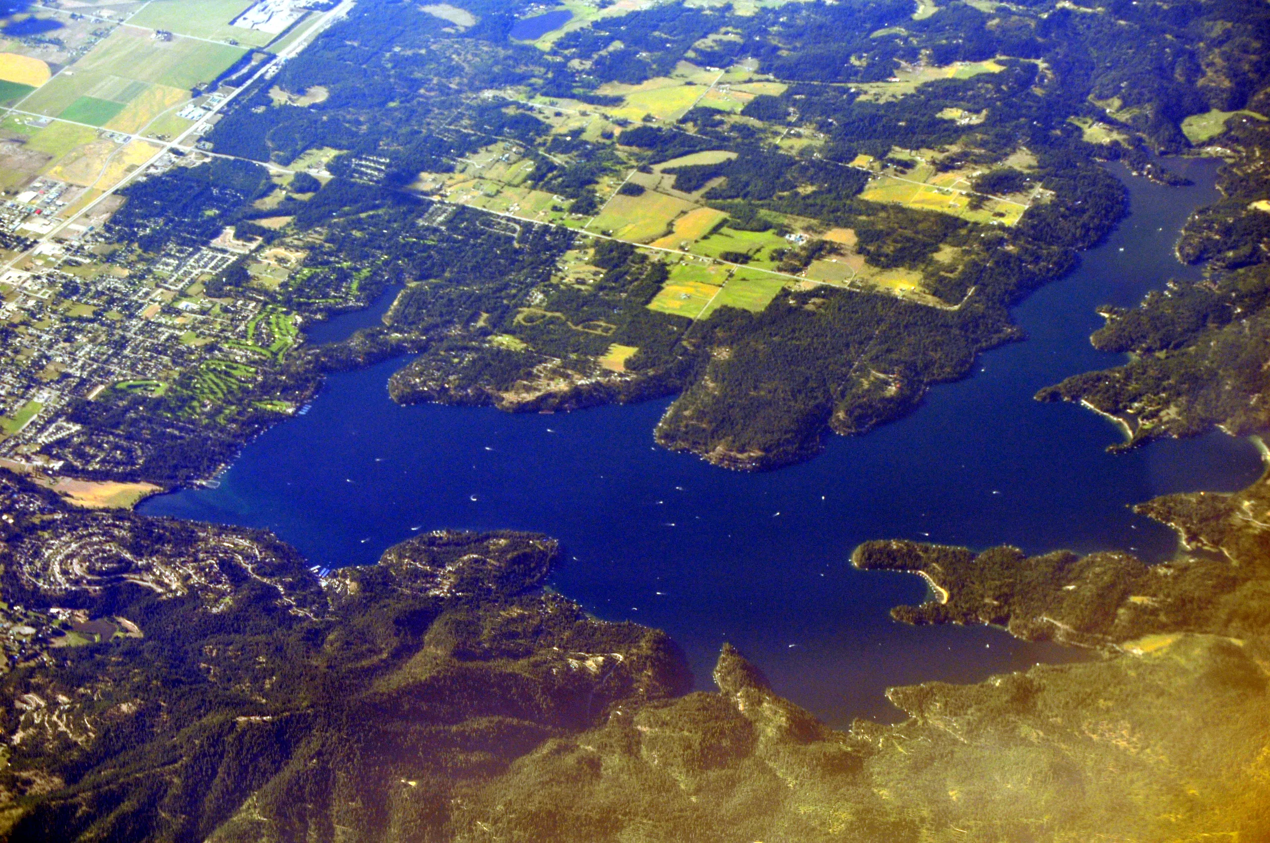 Aerial view of Hayden Lake in Idaho, with deep blue water, forested peninsulas, and the town of Hayden along the west shore.